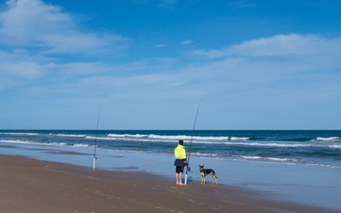 A fisherman and his dog on 90 Mile Beach in Victoria, Australia