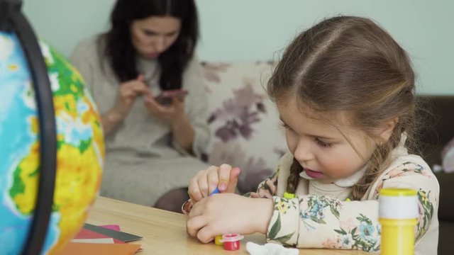 Nice little girl paints a clay craft sitting at table at home