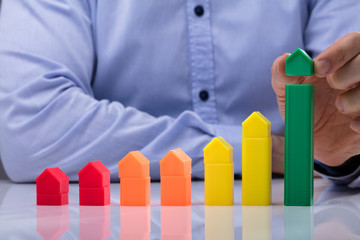 Person Placing Small Green House On Top Of Increasing Graph © Andrey Popov