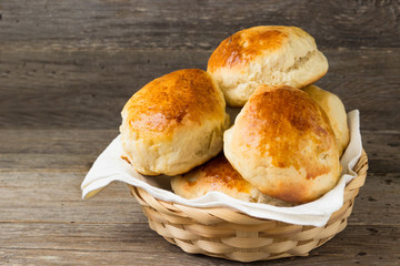 Homemade buns in a basket on a wooden table.
