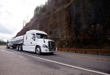 Big rig semi truck tractor transporting tank semi trailer on winding mountain road