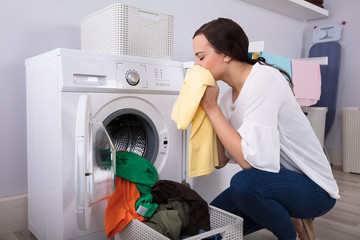 Woman Smelling Cleaned Yellow Cloth Near Washing Machine