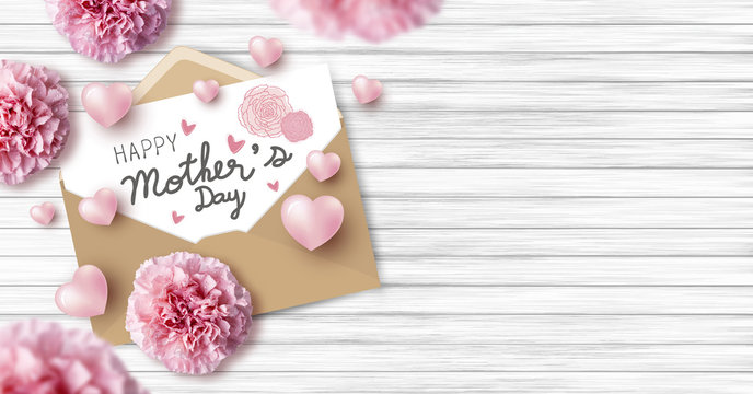 Happy mother's day on white paper in brown envelope and pink heart and carnation flowers on wood texture background with copy space