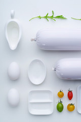Top view of the composition of white dishes and sausages with the addition of multi-colored...
