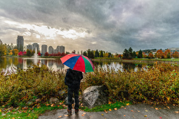 man with an umbrella stands in the rain in a park with a lake