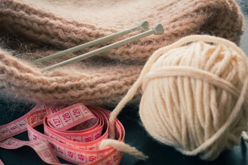 Accessories for knitting. A centimeter tape, a woolen ball, knitting needles and a knitted product.
