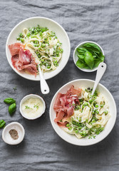 Lunch table in mediterranean style. Fettuccine pasta with creamy sauce, green peas and prosciutto on grey background, top view