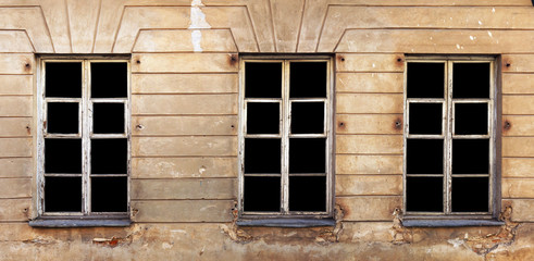 Three wooden  white  windows   in the yellow plastered wall of a ruined old brick house