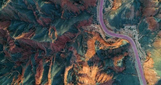 Aerial view on a curved, red road within orange sandstone hills covered with sparse vegetation. Unique, minimalistic landscape in Zhangye Danxia National Geopark, China.