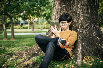 young man using a tablet and sitting under the tree