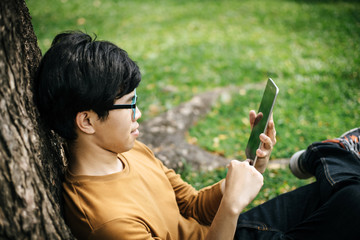 young man using a tablet and sitting under the tree