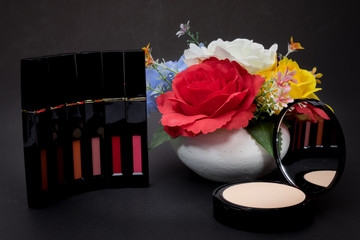 Lipstick,powder and flowers with cosmetics for women To make her look beautiful at work on a black background.