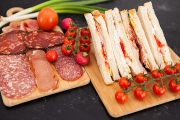 Club sandwiches next to cherry tomatoes, radish and green onion on wooden boards