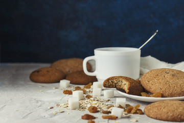 Cup of coffee with milk in a white cup, Bottles with milk, oatmeal cookies, oatmeal, raisins on a light background. Scene from breakfast