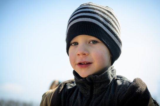 Portrait photo of a caucasian boy in a cap and jacket on a sunny spring day. The boy is playing outside on the playground.