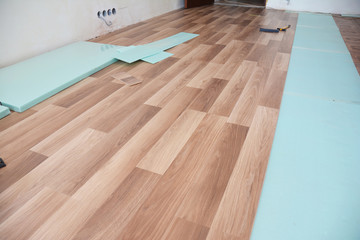 Installing wooden laminate flooring with insulation and soundproofing sheets.