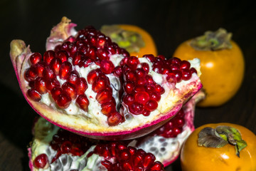 Kitchen still-life. Wholesome ripe fruits of pomegranate and persimmon on a dark brown table.