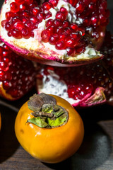 Kitchen still-life. Wholesome ripe fruits of pomegranate and persimmon on a dark brown table.