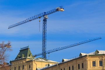 High-rise building cranes on blue sky background and city roofs in sunny winter day