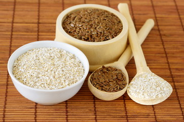 Flax seeds and oat bran in bowls and wooden spoons on bamboo napkin