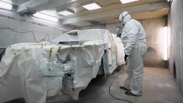 The person in a protective suit is engaged in a color change on the machine, the mechanic uses a spray gun with paint