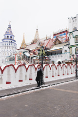 Obraz premium A young beautiful girl in a mink coat and a Russian folk scarf walks around the Izmailovo Kremlin. Moscow, Russia.