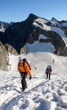 mountain guide and client heading up a glacier towards a high alpine summit on a beautiful summer morning