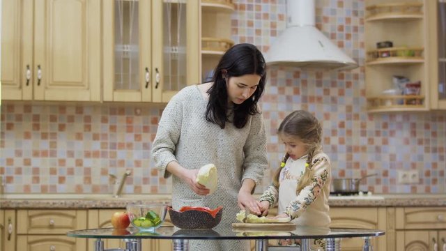 Young woman teaches little daughter to cut cabbage
