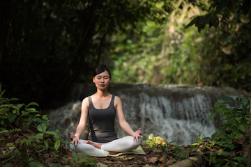 Young woman in yoga pose sitting near waterfall