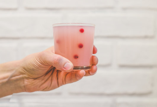 Pink cloudy drink with berries in a glass in a hand on a white background