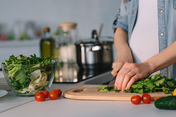 cropped image of attractive pregnant woman cutting vegetables for salad at kitchen