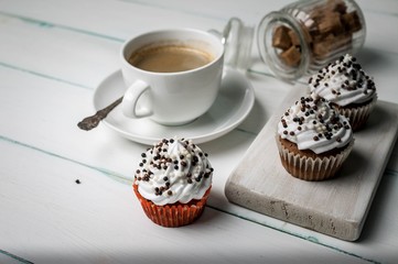 Vanilla cupcakes with chocolate topping and cup of coffee on a wooden chopping board on a light background