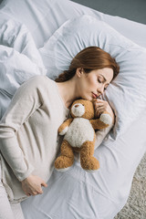 high angle view of attractive pregnant woman sleeping on bed with teddy bear