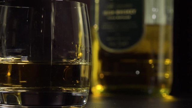 Closeup on a glass of whiskey - a bottle in the blurry background