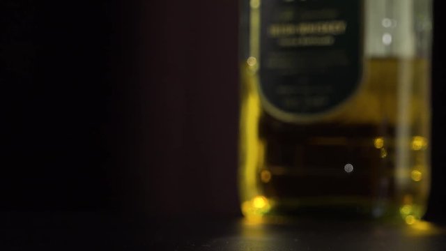 A man lifts a glass of whiskey from a table - closeup - a bottle in the blurry background