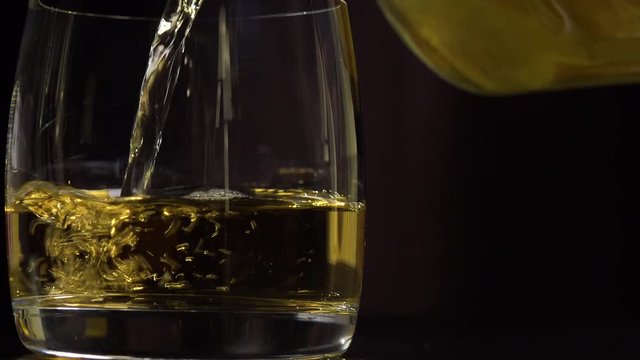 A man pours whiskey into a glass and puts the bottle into the blurry background