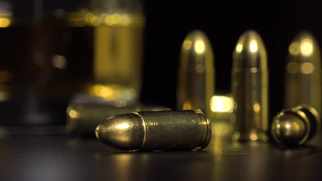 Closeup on bullets on a black table - a glass of whiskey in the blurry background