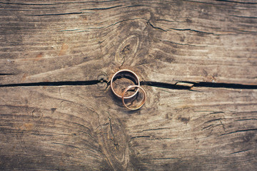 two golden wedding rings lie on a table of dark cracked wood