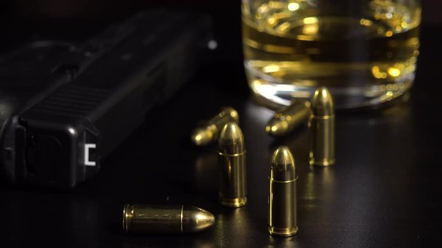 A glass of whiskey, a gun and bullets on a black table - closeup