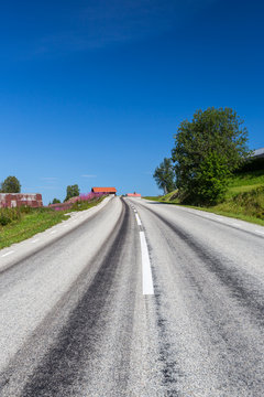 Straight gray asphalt road in country side with old buildings and blue sky.