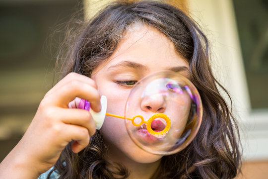 Close up of young caucasian girl child blowing soap bubbles.