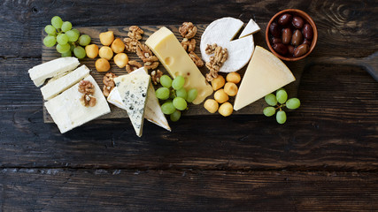 Cheeseboard with various cheeses, fruits and nuts. Dark wooden food background
