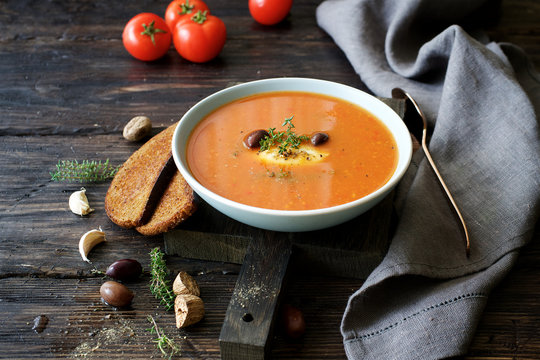 Tomato soup with cheese, olives and herbs. Dark wooden background
