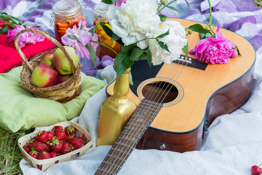 Picnic in the outdoor with guitar, apples, strawberry, beverages, pillows and peonies