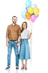 happy couple with colorful balloons holding hands and smiling at camera isolated on white