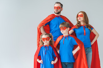 family of superheroes in costumes standing with hands on waist and looking away isolated on grey
