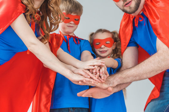 cropped shot of super family in costumes stacking hands together isolated on grey