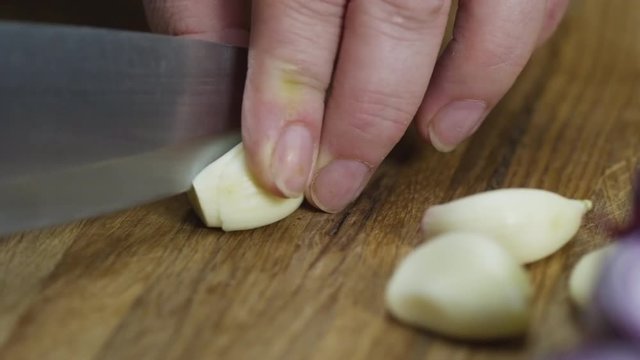 PAN with close up of unrecognizable cook finely chopping garlic cloves on wooden board