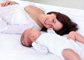 Mother and child lie together, look at each other with love. View from top above of affectionate mom and newborn. Young woman and her baby faces. Children and parents concept
