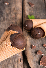 Chocolate ice cream scoop in cone on wooden table. Sweet desert.